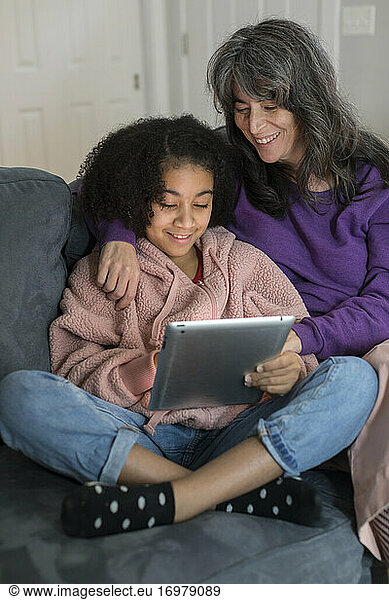 Caucasian mother and bi-racial pre-teen daughter look at ipad together