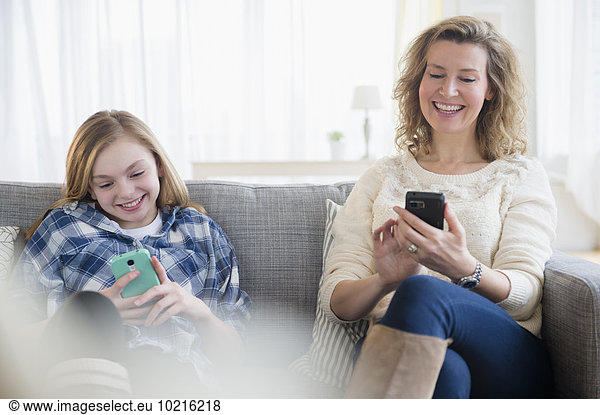 Caucasian mother and daughter using cell phones on sofa