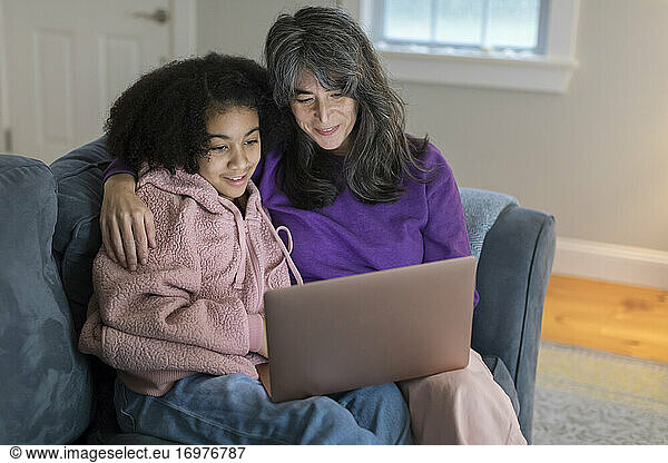 Caucasian mother  bi-racial daughter on couch watching movie together