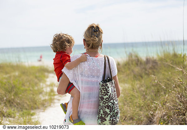 Caucasian mother carrying baby son on beach