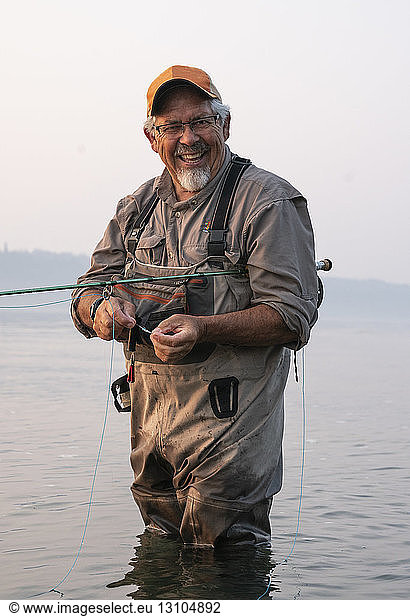 Caucasian senior male tying a fly on his fly fishing line while fishing for salmon and searun cutthroat trout