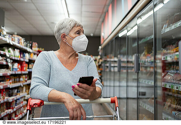 Caucasian senior woman with face mask and telephon shop in supermarket