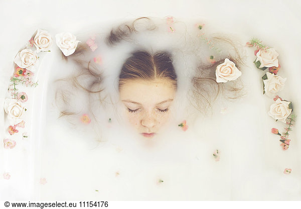 Caucasian teenage girl floating in milk bath with flowers