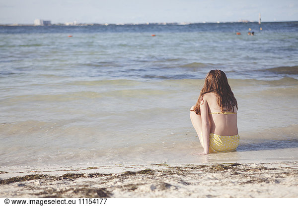 Caucasian teenage girl sitting in waves on beach