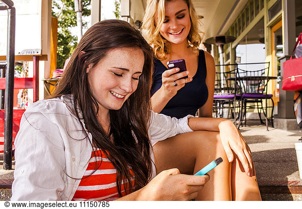Caucasian teenage girls using cell phones in city