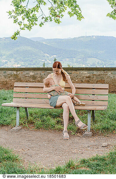 Caucasian woman breastfeeding her baby girl in the park of Bergamo