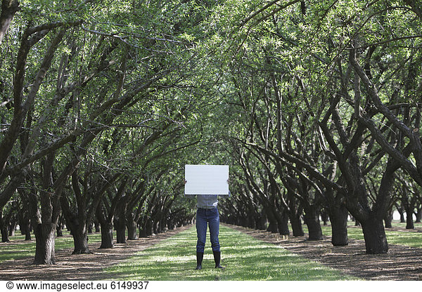 Caucasian woman holding blank placard underneath trees