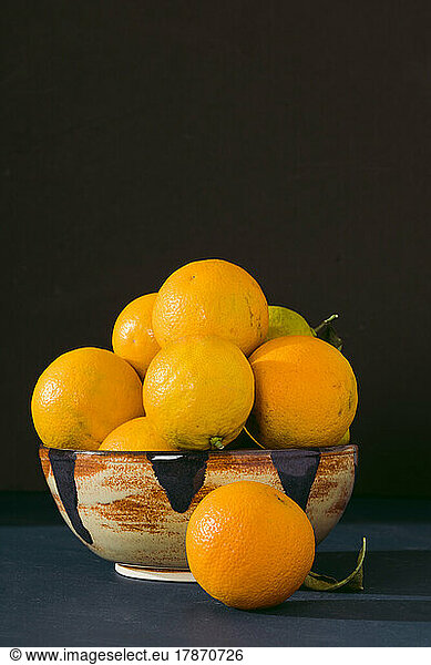Ceramic bowl filled with fresh Valencia oranges against black background
