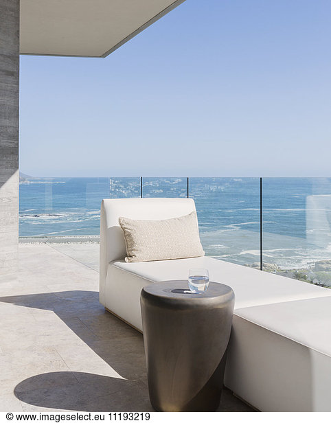 Chaise lounge and water glass on sunny luxury balcony with ocean view