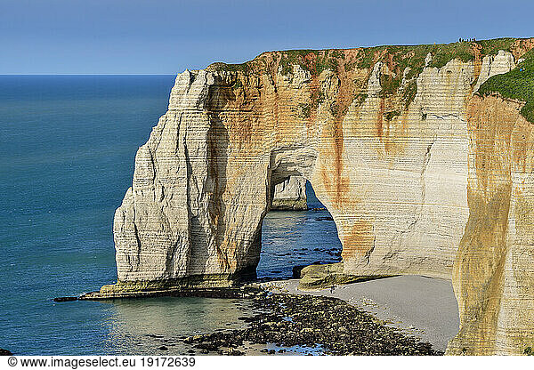 Chalk cliffs with natural arch on sunny day near blue sea