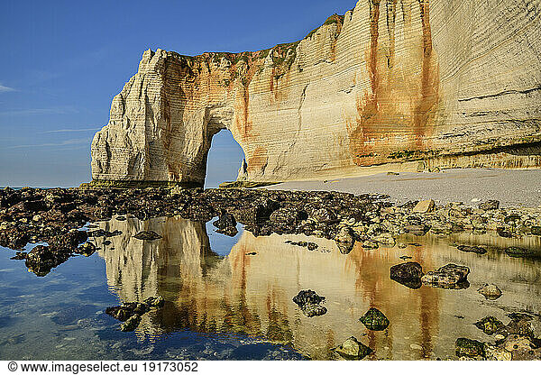 Chalk cliffs with natural arch on sunny day near rocky coastline
