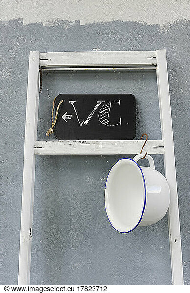 Chamber pot hanging on ladder holding chalkboard restroom sign