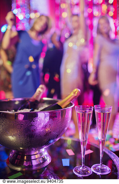 Champagne bottles in ice bucket and champagne flutes in nightclub  people dancing in background
