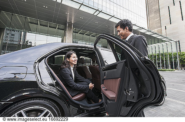 chauffeur opening car door for business woman at office building