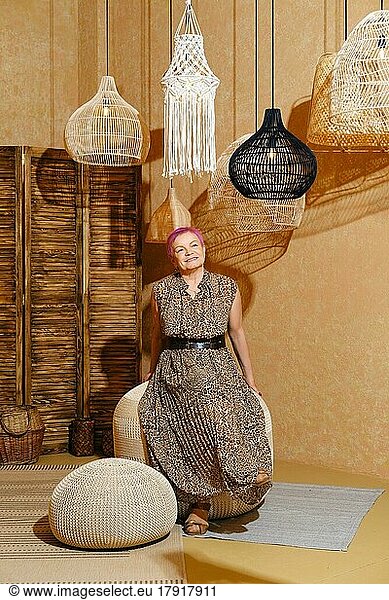 Cheerful and careless old woman with pink hair sitting on wicker padded stool
