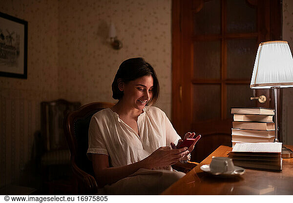 Cheerful bookworm using smartphone near books