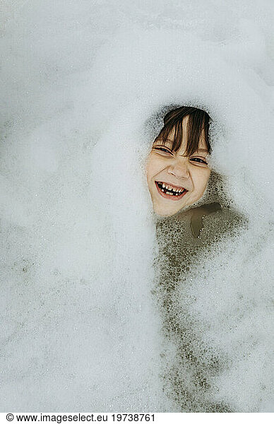 Cheerful boy amidst soap sud in bathtub