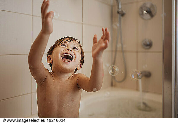 Cheerful boy bathing and enjoying with soap bubbles in bathtub