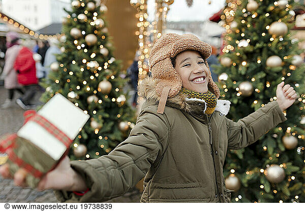 Cheerful boy holding gift box and enjoying at Christmas market
