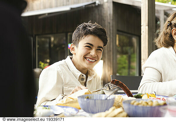 Cheerful boy sitting at dining table in patio during dinner party