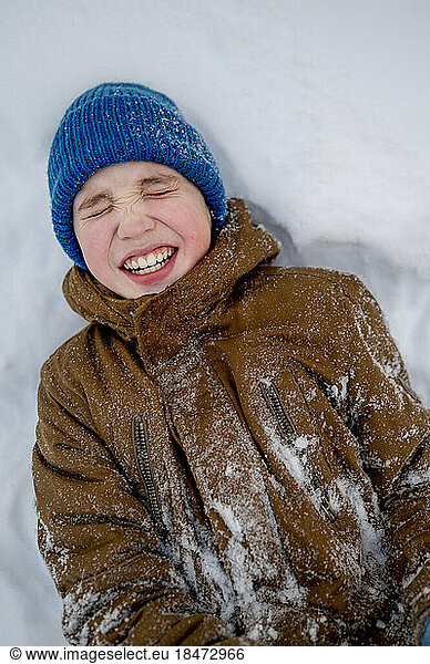 Cheerful boy wearing blue knit hat lying on snow