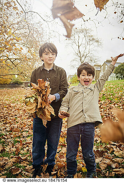 Cheerful boys throwing away autumn leaves at park