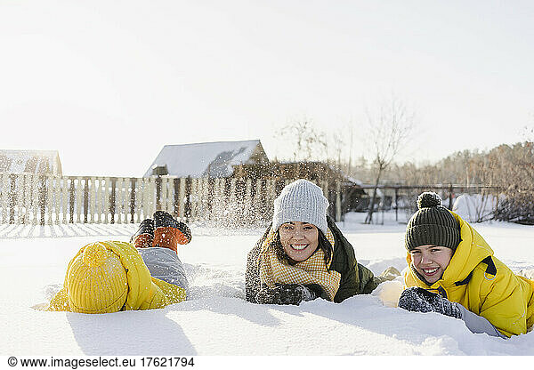 Cheerful boys with mother lying on snow in winter