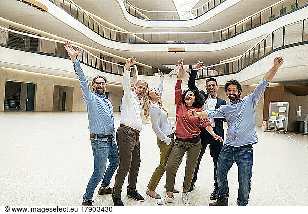 Cheerful business colleagues with arms raised standing in lobby
