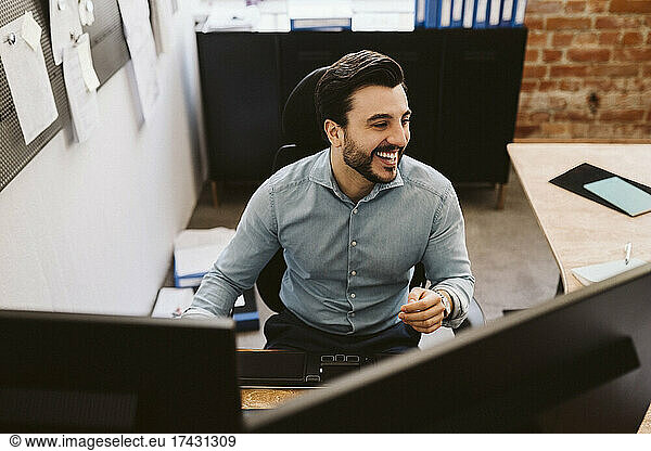 Cheerful business man sitting at desk while looking away