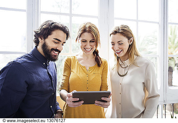Cheerful business people using tablet computer against windows