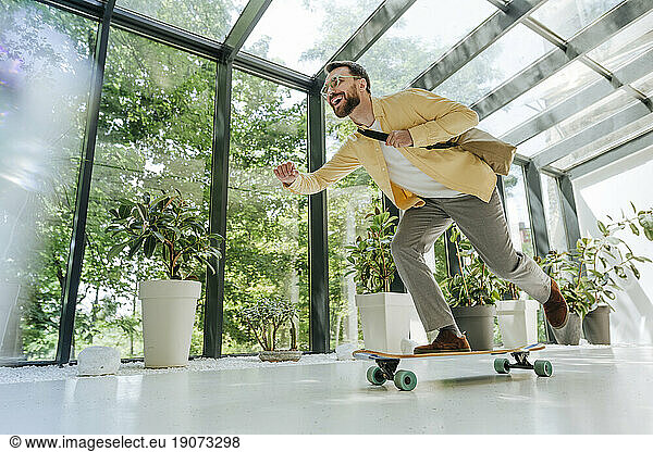 Cheerful businessman enjoying longboard skating in office