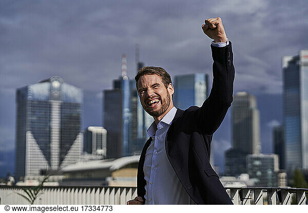 Cheerful businessman with hand raised celebrating at building terrace