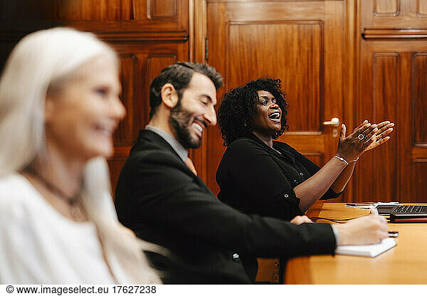 Cheerful businesswoman clapping while sitting by colleagues in board room meeting
