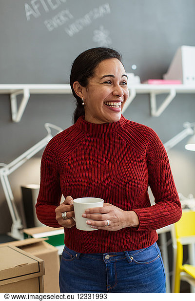 Cheerful businesswoman holding coffee cup while looking away against wall at creative office