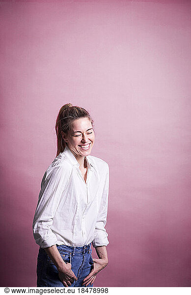 Cheerful businesswoman standing against pink background