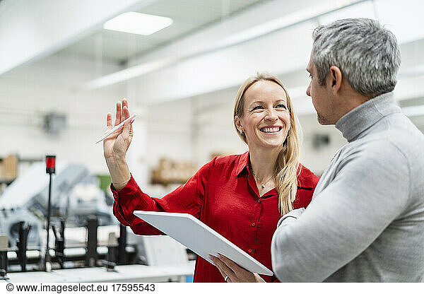 Cheerful businesswoman with tablet PC sharing ideas with colleague in factory