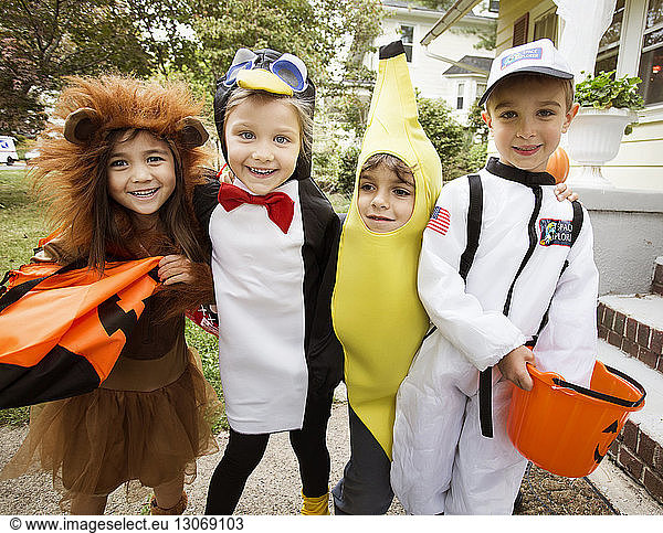 Cheerful children in Halloween costumes standing by house during trick or treating