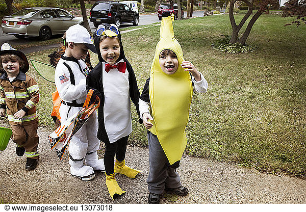 Cheerful children in Halloween costumes standing on pathway during trick or treating