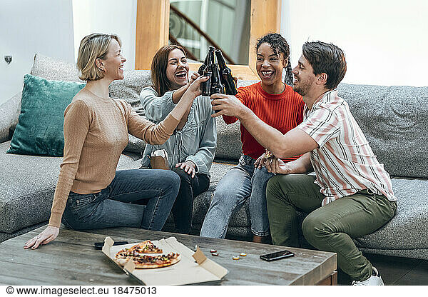 Cheerful colleagues toasting beer bottles on sofa at office
