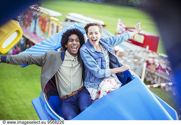 Cheerful couple having fun on carousel in amusement park