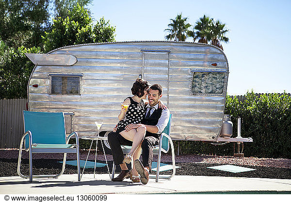 Cheerful couple sitting on chair against camper van