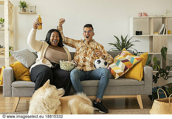 Cheerful couple watching TV and enjoying beer at home