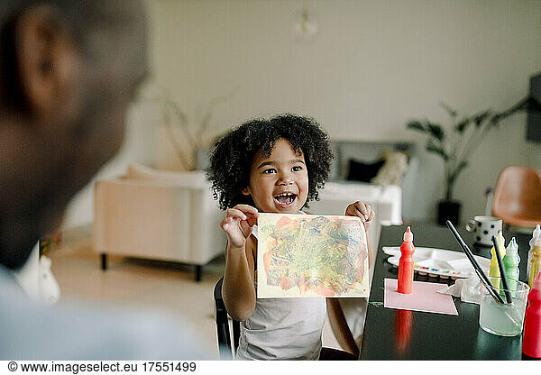 Cheerful daughter showing painting to father at home