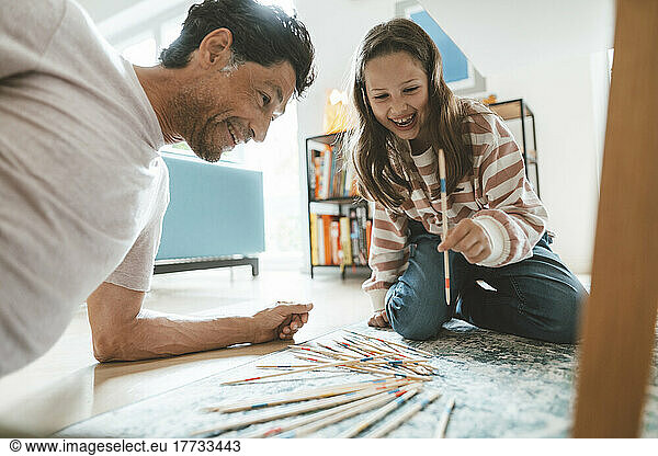 Cheerful daughter with father playing mikado at home