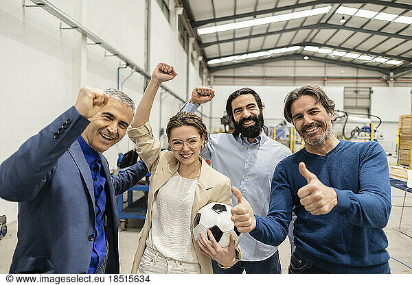 Cheerful engineers cheering together with colleague showing thumbs up gesture in industry