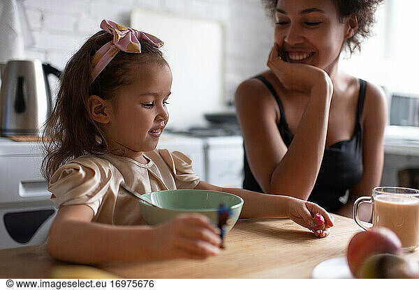 Cheerful ethnic girl playing during breakfast with mother