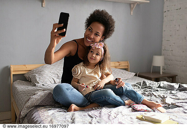 Cheerful ethnic mother with daughter making video call on smartphone