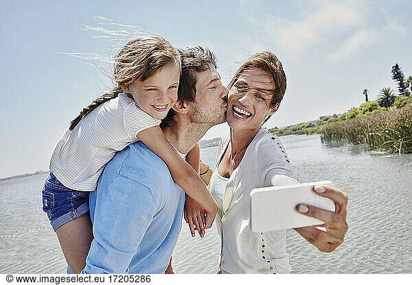 Cheerful family taking selfie through mobile phone by lake