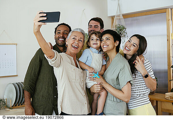 Cheerful family taking selfie with smart phone in kitchen