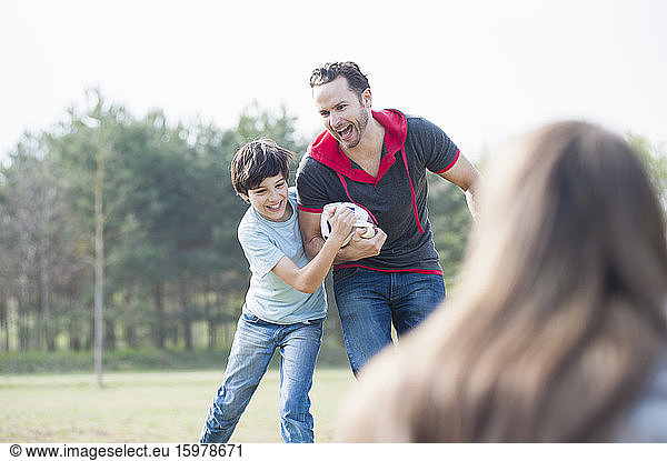 Cheerful father and son playing rugby with woman in foreground at park